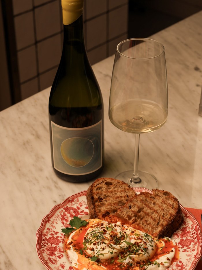 Botella y copa de vino blanco junto a un plato de burrata en Chez Janou
