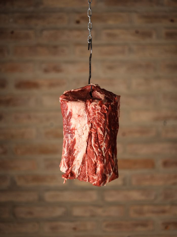 Un corte de carne colgado de un gancho frente a una pared de ladrillo