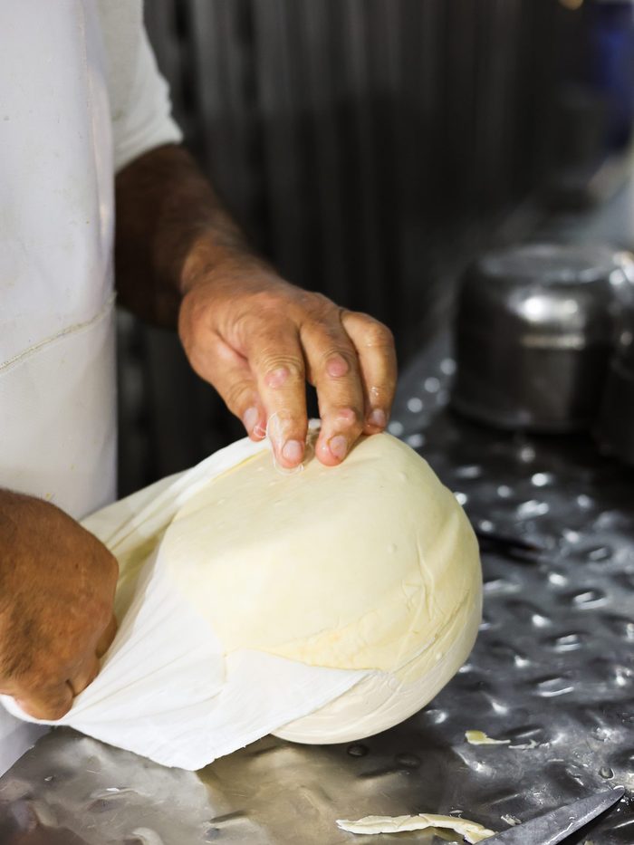 Detalle de proceso: unas manos moldean una horma de queso recién cuajada