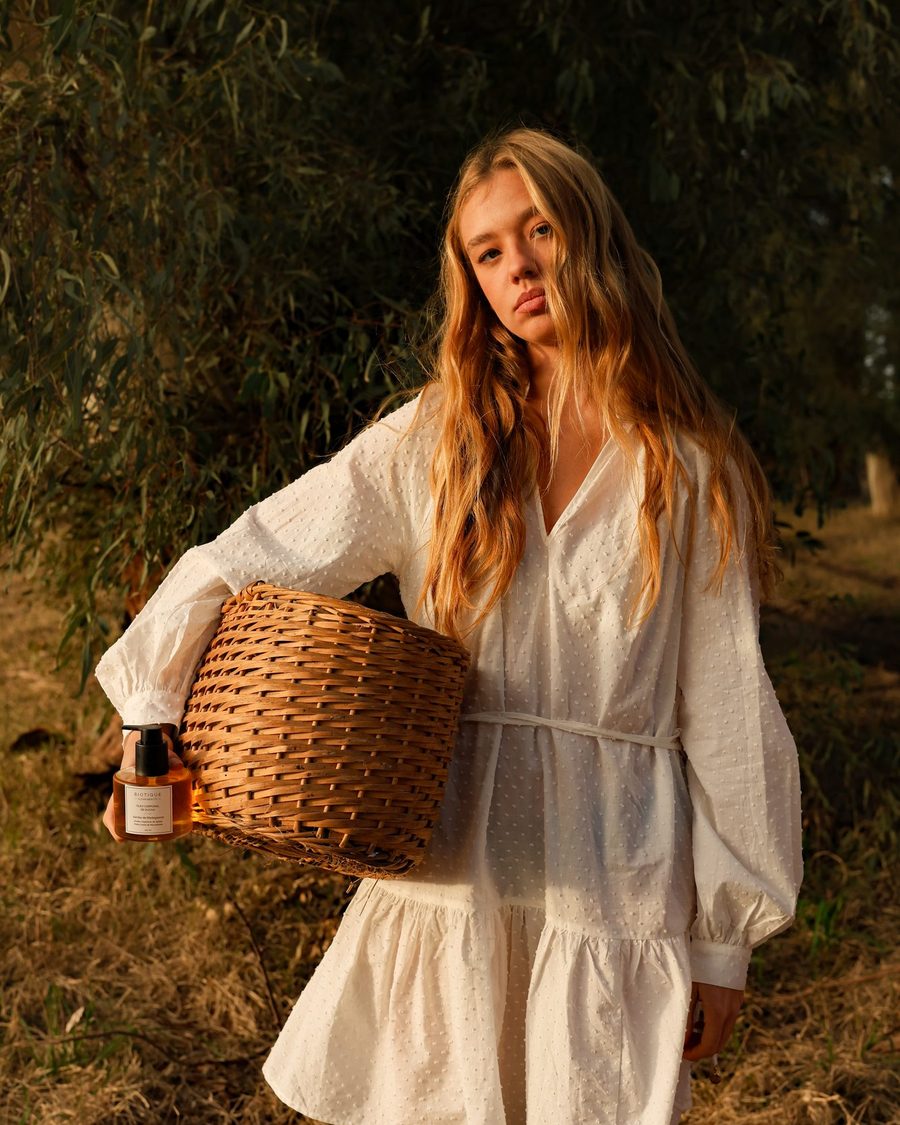 Escena de marca al atardecer: la modelo camina por el campo con una canasta de productos